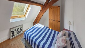 A bedroom with a sloped ceiling, a wooden wardrobe, a bed with striped bedding, a framed picture on the wall, and a skylight.