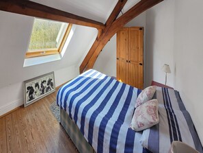 A bedroom with a sloped ceiling, a wooden wardrobe, a bed with striped bedding, a framed picture on the wall, and a skylight. - St Albans Church - 28165 (Treherbert, near Treorchy)