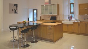 A modern kitchen with a central island, bar stools, wooden cabinets, and a large window.