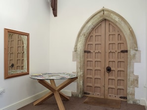 Een kamer met een ronde glazen tafel, een houten deur met een stenen boog en een spiegel aan de muur.