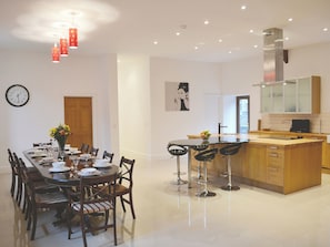 A modern kitchen with a central island, a dining area with a long table and chairs, and a visible clock on the wall. - St Albans Church - 28165 (Treherbert, near Treorchy)