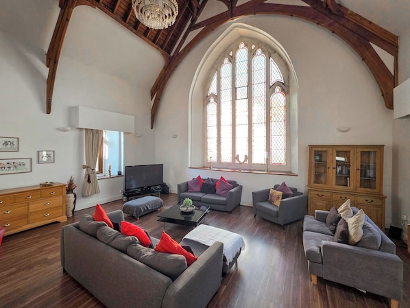 A spacious living room with wooden beams, a large arched window, and modern furniture.