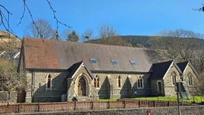 A stone church with a tiled roof, arched windows, and a wooden fence in front.
