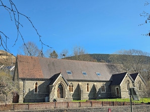 A stone church with a tiled roof, arched windows, and a wooden fence in front.