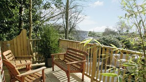 Une terrasse en bois avec un banc et des chaises, entourée de plantes et d’une clôture en bois.