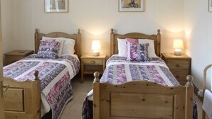 A double room with two wooden beds, each with a nightstand and a lamp. There are framed pictures on the wall above the beds.