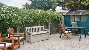 A patio area with a wooden bench, two chairs, a table, and a small shed.