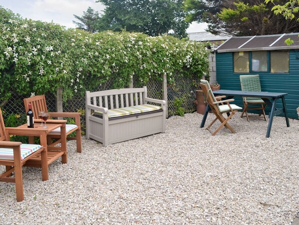 Een terras met een houten bank, twee stoelen, een tafel en een kleine schuur.