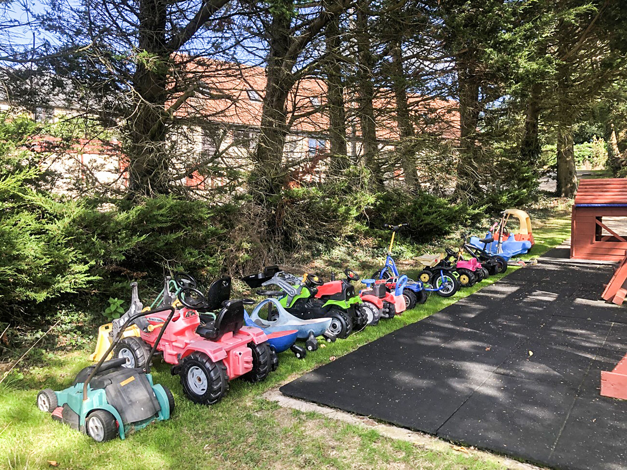 Eine Reihe bunter Spielzeugfahrzeuge, abgestellt auf einer Wiese neben einem befestigten Weg.