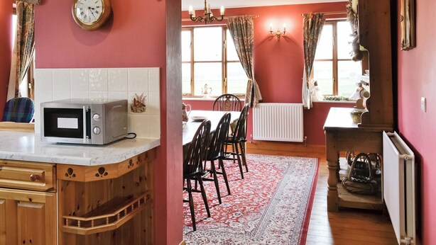 Een keuken met een magnetron, een klok en een bakstenen boog die leidt naar een eethoek met een tafel en stoelen.