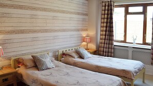 Een kamer met twee houten bedden, een nachtkastje met een lamp en een raam met gordijnen.