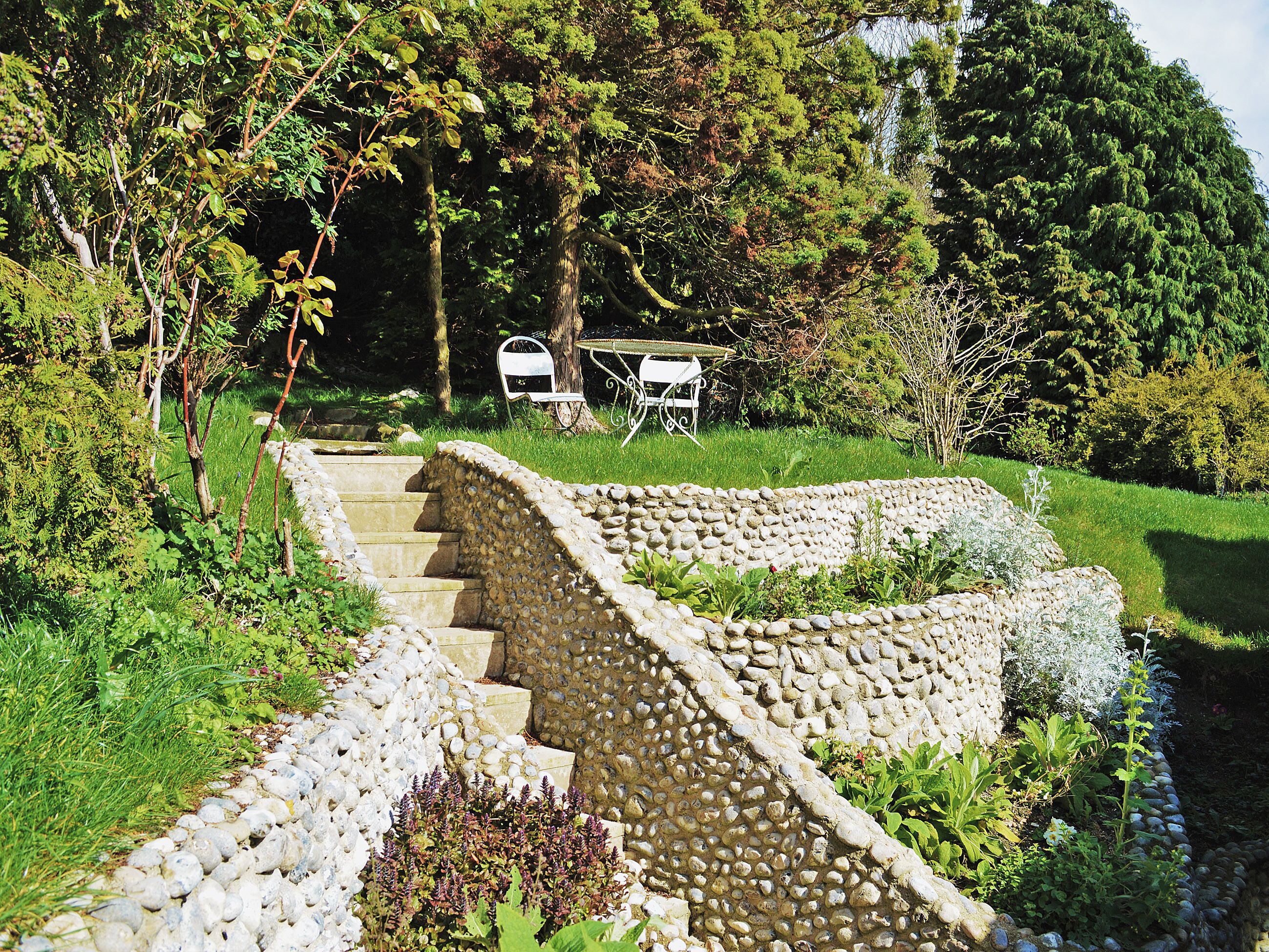 A stone staircase leading up to a garden area with a table and chairs.