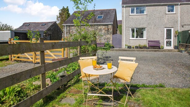 A courtyard with a wooden fence, a table with chairs, and a bench. There are houses in the background. - 2 bedroom accommodation in Bodffordd, near Llangefni (Bodffordd, near Llangefni)