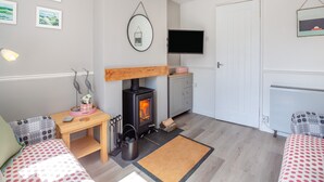 A cozy living room with a fireplace, a television mounted on the wall, and a comfortable seating area with patterned cushions. - 2 bedroom accommodation in Bodffordd, near Llangefni (Bodffordd, near Llangefni)
