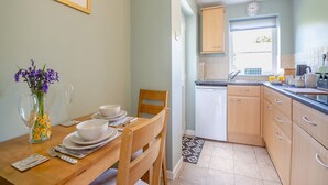 A dining table with white plates and bowls, a vase with flowers, and a glass of water. - 2 bedroom accommodation in Bodffordd, near Llangefni (Bodffordd, near Llangefni)