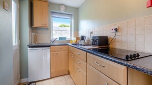 A compact kitchen with wooden cabinets, a built-in dishwasher, a microwave, and a window providing natural light. - 2 bedroom accommodation in Bodffordd, near Llangefni (Bodffordd, near Llangefni)