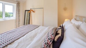 A neatly made bed with patterned bedding, a bedside table with a lamp, a window with curtains, and a mirror on the wall. - 2 bedroom accommodation in Bodffordd, near Llangefni (Bodffordd, near Llangefni)