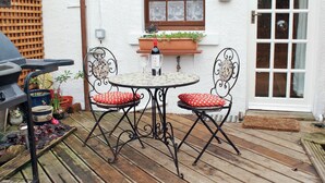 Eine Terrasse mit einem runden Tisch, zwei Stühlen, einem Grill und Topfpflanzen.