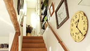 Eine Treppe mit hölzernem Geländer führt zu einer Zwischenebene, wo eine wandmontierte Uhr und gerahmte Bilder zu sehen sind.