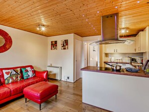 A modern kitchen with wooden ceiling, a red leather sofa, and a small island with a sink. - Strawberries And Cream (Bowness on Windermere)