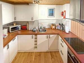 A compact kitchen with white cabinets, a wooden countertop, a stainless steel sink, and a microwave. - Strawberries And Cream (Bowness on Windermere)