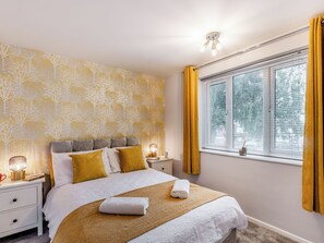 A neatly made bed with a white and brown blanket, a bedside lamp, and a nightstand with a book and a cup. - Strawberries And Cream (Bowness on Windermere)