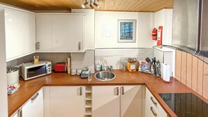 Une cuisine de taille réduite avec des meubles blancs, un plan de travail en bois, un évier en acier inoxydable et un four à micro-ondes.
