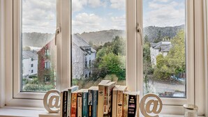 Une fenêtre donnant sur une ville et une rangée de livres posée sur un rebord de fenêtre.