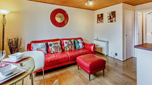 A cozy living room with a red leather sofa, a dining table with white plates, and a wooden ceiling.