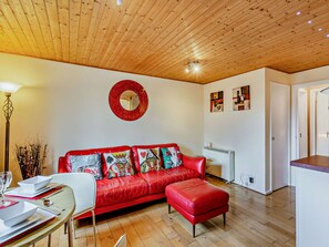 Una sala de estar acogedora con un sofá de cuero rojo, una mesa de comedor con platos blancos y un techo de madera.