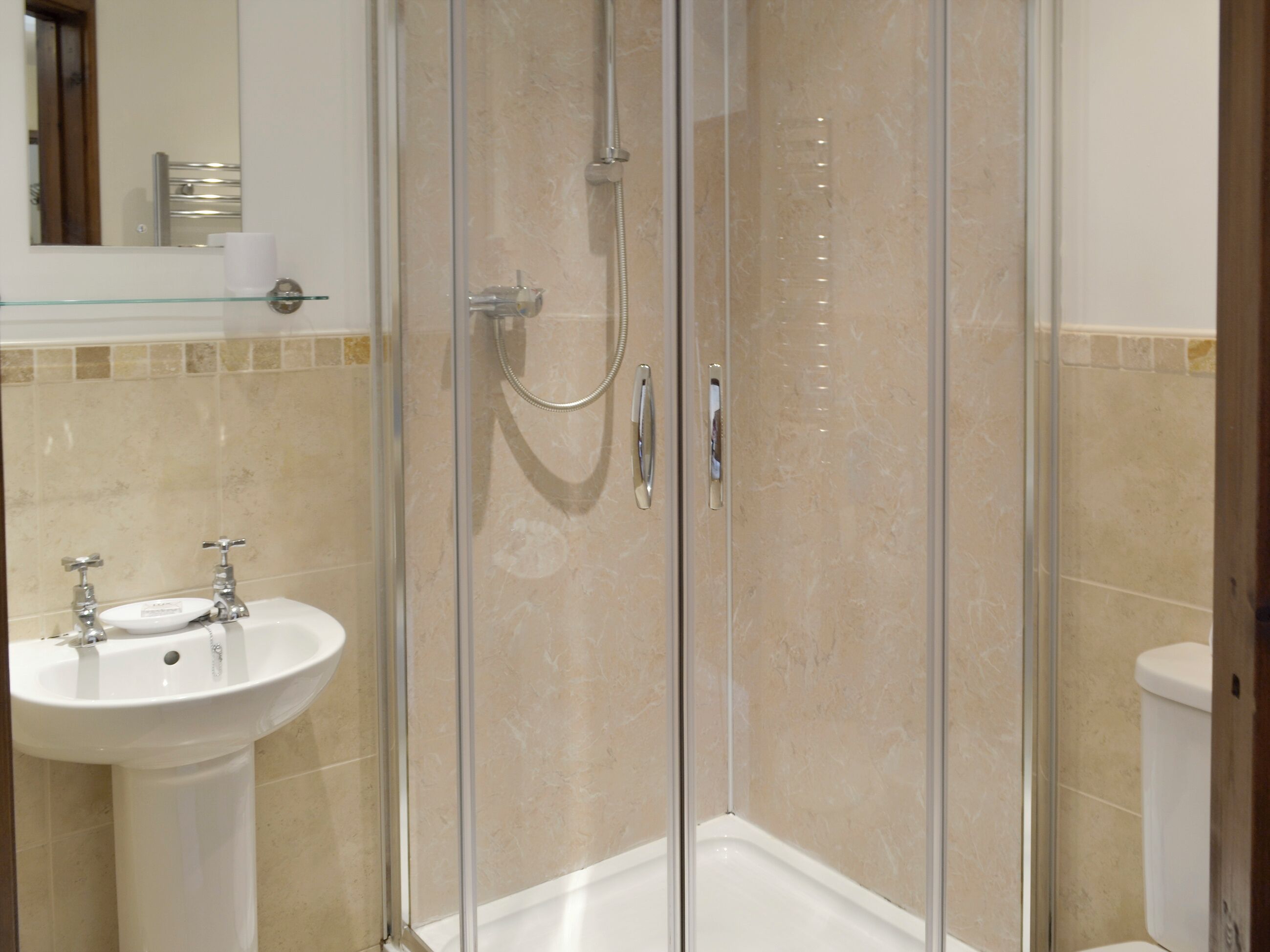 Un baño con ducha de vidrio, lavamanos pedestal y un inodoro.