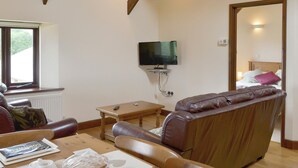 A living room with a wooden ceiling, a television mounted on the wall, a sofa, a table, and a window.