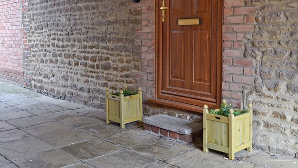 A wooden door with a brass handle, a brick wall, and two wooden planters with greenery. - 3 bedroom accommodation in Snettisham, near Hunstanton (Snettisham, near Hunstanton)