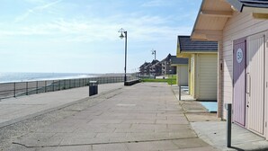 Un paseo marítimo con una hilera de cabañas de playa, una barandilla de metal y una vista despejada del mar.