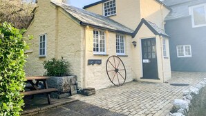 Una cabaña tradicional con chimenea de piedra, una noria grande y un cartel que dice 'Liam Cottage'.