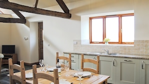 A dining area with a wooden table set for four, a kitchen with a window, and a television in the corner.