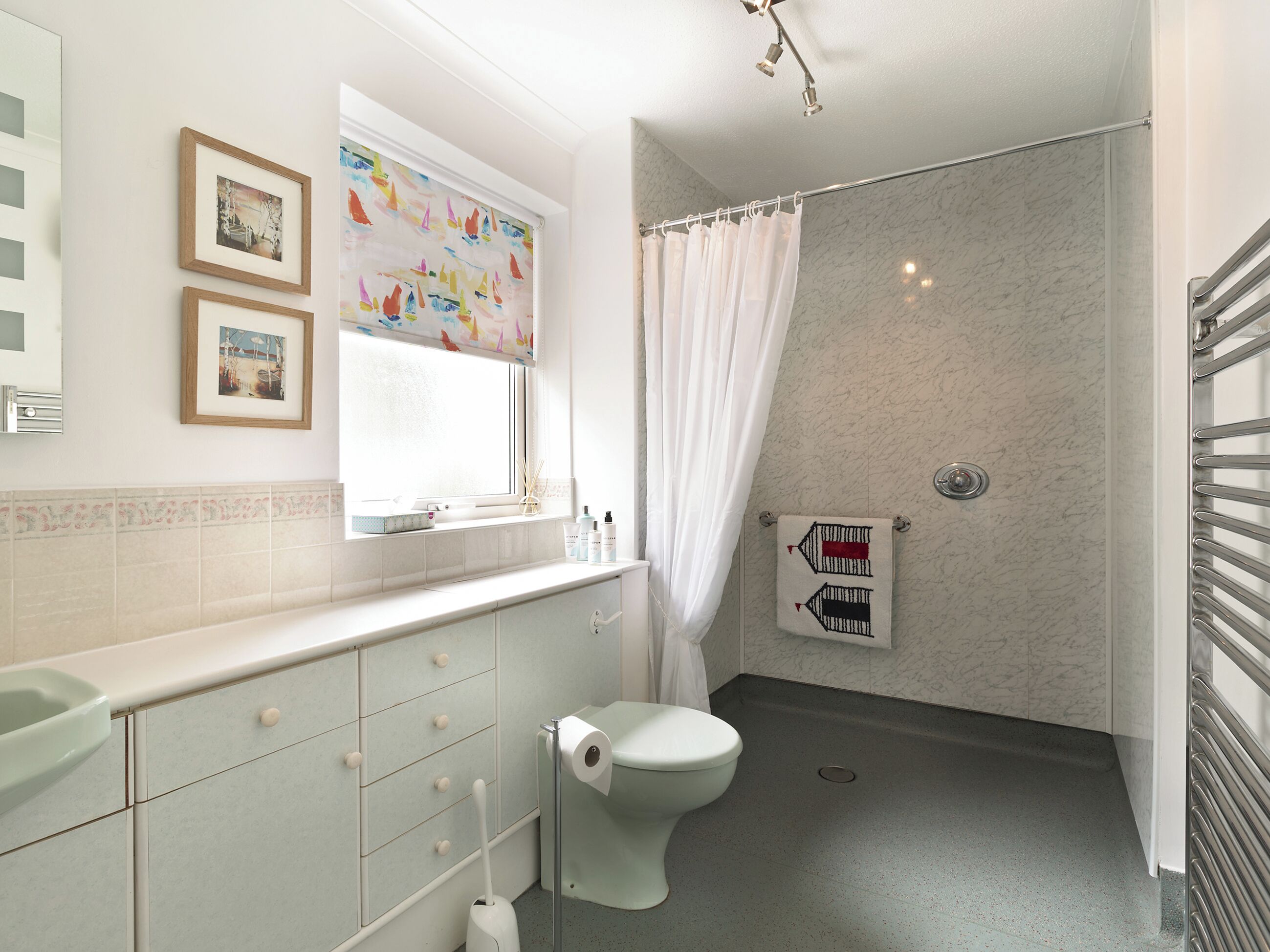 A bathroom with a toilet, a shower with a curtain, a window with artwork, and a towel rack with a towel.