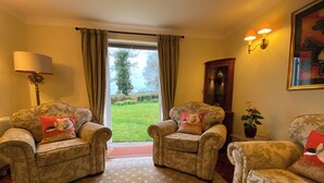 A living room with two armchairs, a floor lamp, a potted plant, and a view of a garden through a glass door. - 3 bedroom accommodation in Misterton, near Crewkerne (Misterton, near Crewkerne)
