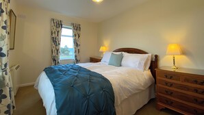 A bedroom with a bed, two bedside tables with lamps, a window with curtains, and a wooden dresser. - 3 bedroom accommodation in Misterton, near Crewkerne (Misterton, near Crewkerne)