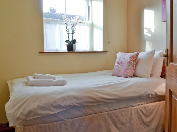 A neatly made bed with white linens, a floral pillow, and a window with a view of buildings. - 3 bedroom accommodation in Carperby, near Leyburn (Carperby, near Leyburn)