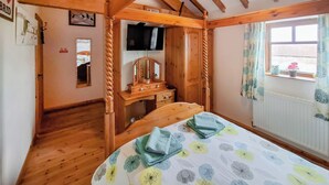 Une pièce chaleureuse avec des poutres apparentes, un lit recouvert d’une couvre-lit à motifs floraux, une télévision et une fenêtre avec des rideaux.