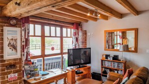 Un salon confortable avec une télévision, des étagères à livres, un canapé en cuir et une vue sur l’extérieur.