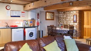 Un salon chaleureux avec un canapé en cuir marron, un lave-linge, une table à manger avec des chaises et un mur en pierre.