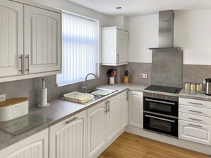 A modern kitchen with white cabinetry, a built-in oven, a stainless steel range hood, and a window with blinds.