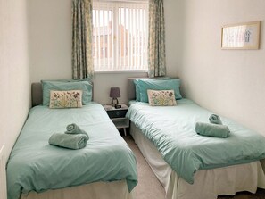 A twin room with two beds, a nightstand, a lamp, and a window with curtains.