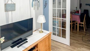 Ett vardagsrum med en platt-TV, en lampa och en matplats med ett bord och stolar.