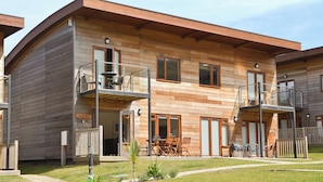 A wooden cabin with a balcony, a small garden, and a wooden deck.