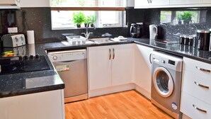 A modern kitchen with a dishwasher, washing machine, and a window with blinds.