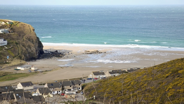 A coastal town with houses on a cliff overlooking the sea, a sandy beach, and a clear view of the ocean.