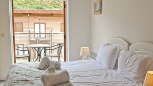 A bedroom with a bed, pillows, a bedside lamp, and a view of an outdoor area with a table and chairs.